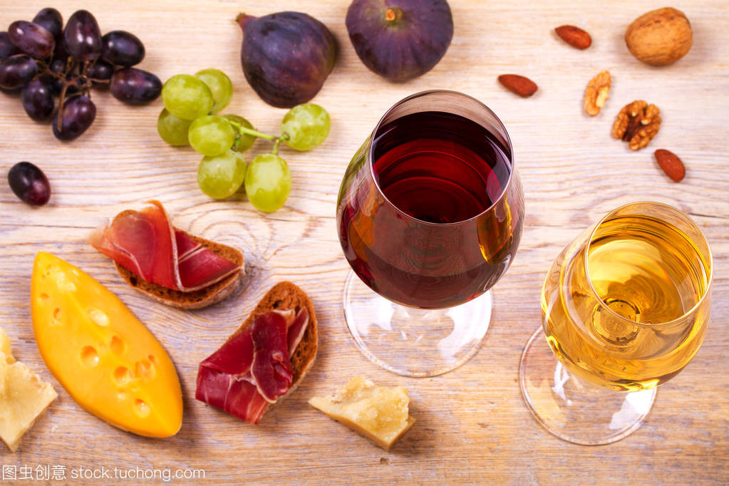 紅色和白色奶酪、 火腿、 無花果和葡萄與葡萄酒杯。木制的桌子上的酒杯。葡萄酒的靜物
